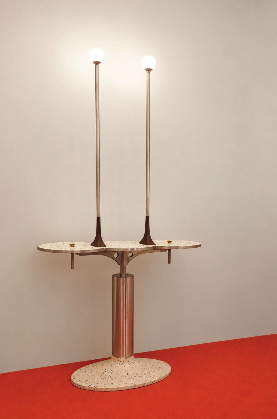 Afterglow cocktail console: a pink terrazzo base and steel column carrying a three-lobed terrazzo top and two tall lamp stems with glowing globes