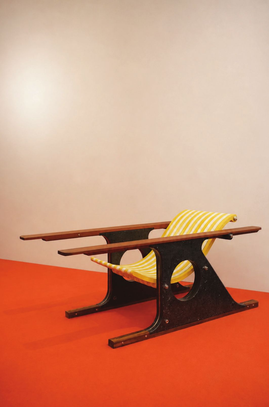 The Daydreamer lounge chair: graphite-black terrazzo side frames with round cut-outs, long teak arms and a yellow and white striped concrete sling seat